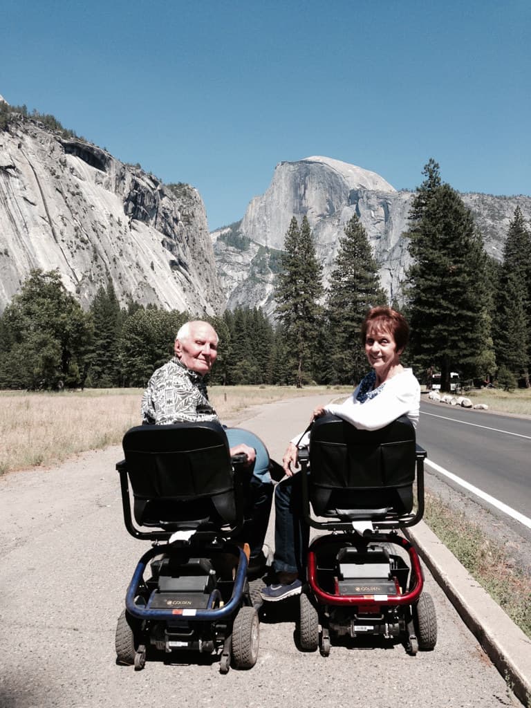Grandma and Papa on mobility scooters in Yosemite Valley with Half Dome behind them